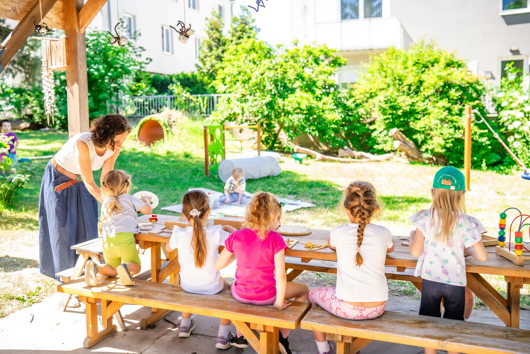 Děti u dřevěného stolu na zahradě školky s paní učitelkou