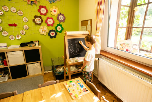 Chlapec kreslí křídou na tabuli u okna do zahrady