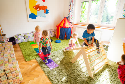 Děti v pohybovém koutku lezou po dřevěné prolézačce, vedle stan a barevné podložky